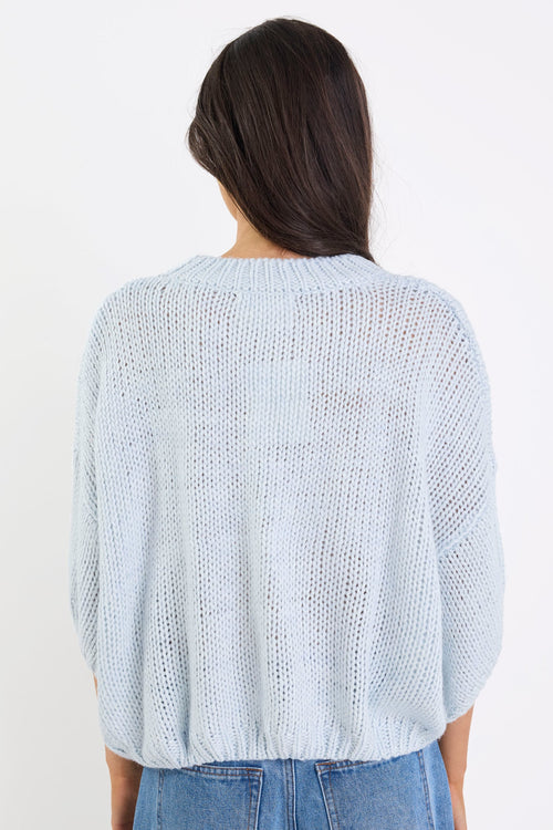 Person wearing a light blue textured sweater and jeans on a white background