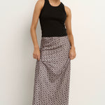 Woman wearing a blush and black geometric print satin midi skirt with a black tank and sneakers.







