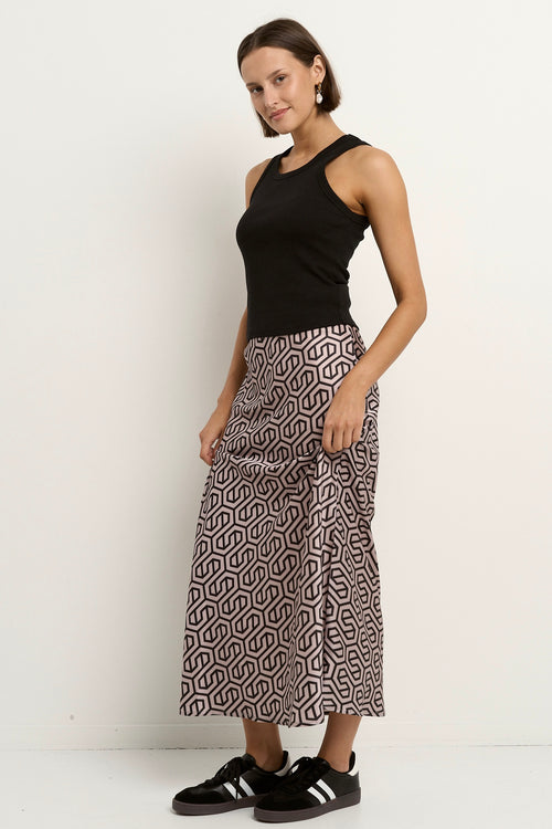 Woman wearing a blush and black geometric print satin midi skirt with a black tank and sneakers.







