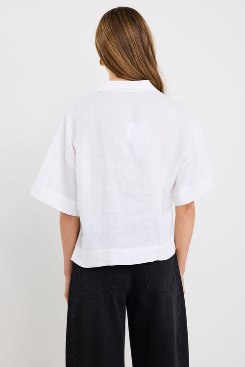 Woman wearing an ivory short sleeve linen shirt with tie-front fastening, styled with high-waist black jeans.
col_pattern