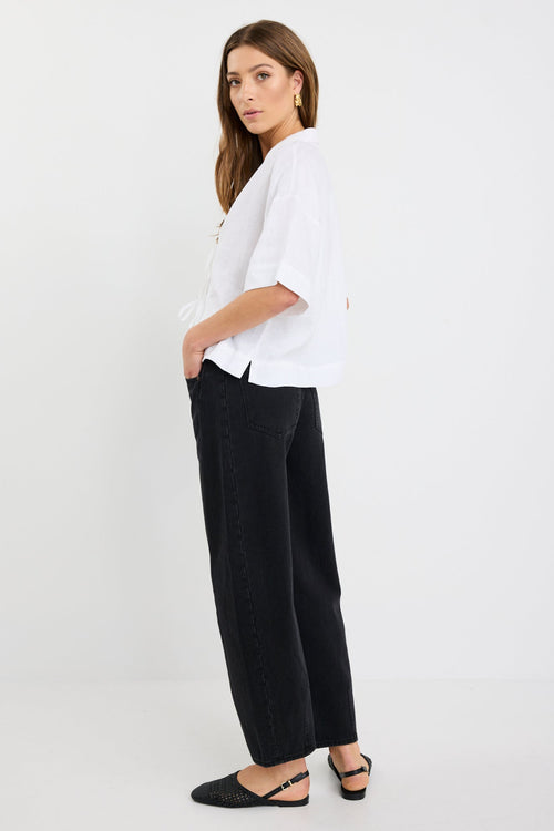 Woman wearing an ivory short sleeve linen shirt with tie-front fastening, styled with high-waist black jeans.