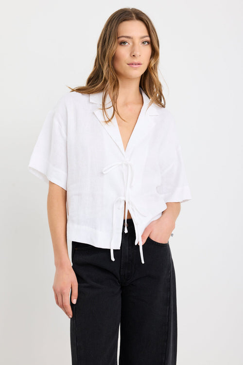 Woman wearing an ivory short sleeve linen shirt with tie-front fastening, styled with high-waist black jeans.