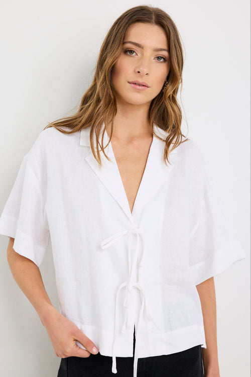 Woman wearing an ivory short sleeve linen shirt with tie-front fastening, styled with high-waist black jeans.