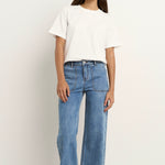 Woman wears a white tee with mid-rise, wide-leg blue jeans featuring front patch pockets and a relaxed silhouette.