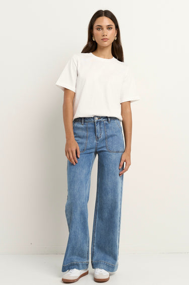 Woman wears a white tee with mid-rise, wide-leg blue jeans featuring front patch pockets and a relaxed silhouette.