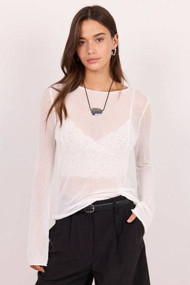 A woman modeling a white sheer long-sleeve mesh top over a white lace bralette, paired with black wide-leg pants, against a plain light background.