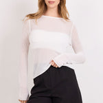 A woman modeling a white sheer long-sleeve top and black shorts against a plain white studio background.