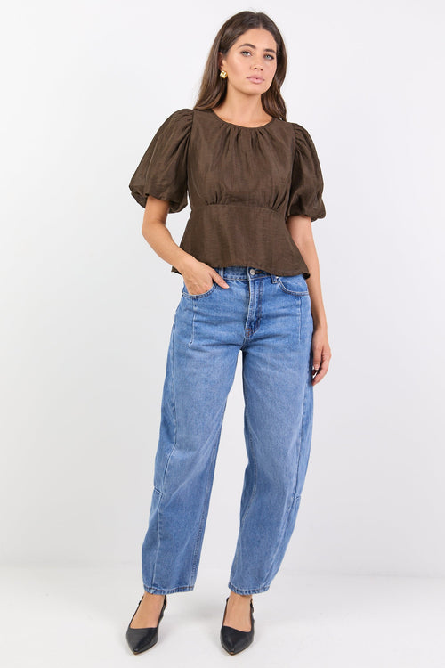 Woman wearing a brown top and blue jeans on a white background