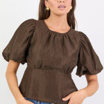 Woman wearing a brown blouse with puffed sleeves and blue jeans on a white background