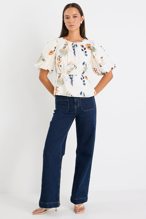 Woman wearing a multicolour cream top with puff sleeves paired with blue jeans