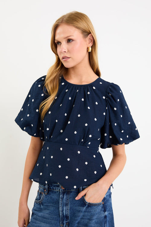 Model wearing a navy short sleeve bubble-sleeve top with white polka dots