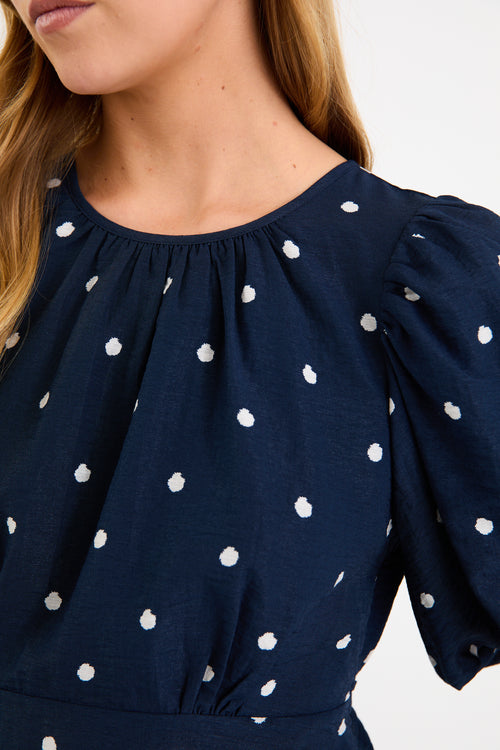 Model wearing a navy short sleeve bubble-sleeve top with white polka dots