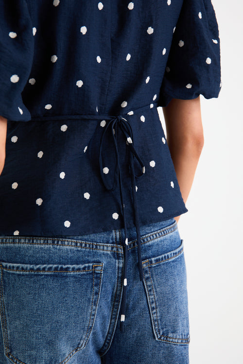 Model wearing a navy short sleeve bubble-sleeve top with white polka dots