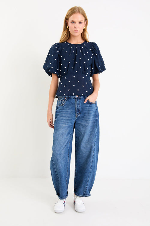 Model wearing a navy short sleeve bubble-sleeve top with white polka dots