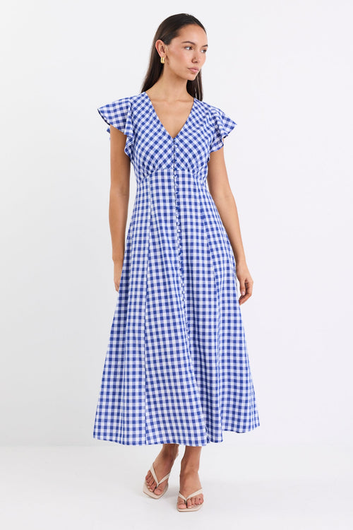 Woman wearing a blue gingham midi dress with a V-neck, button-down front, and fluted sleeves, paired with nude sandals.
