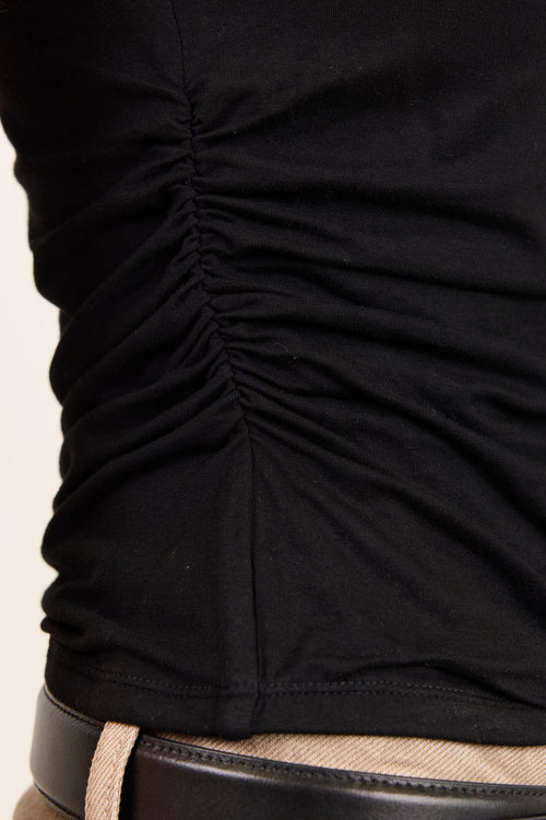 Close-up of a black ruched tank top worn with beige pants and a black belt.