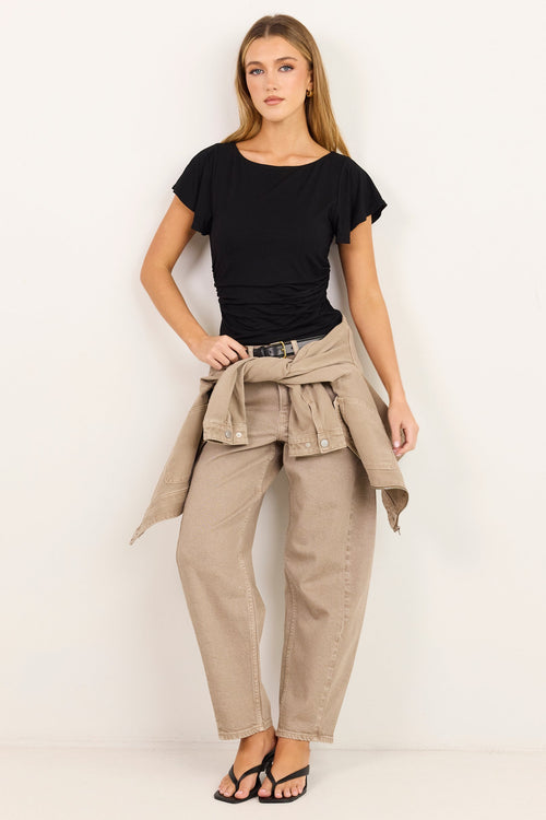 A woman modeling a black short-sleeve t-shirt, beige wide-leg pants, and a matching beige jacket tied around her waist, standing against a plain white studio background.