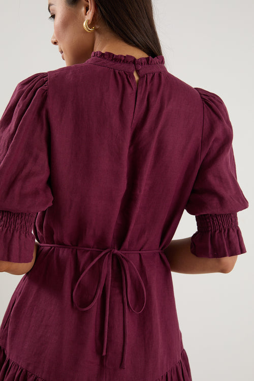 Woman wearing a short plum puff-sleeve mini dress with a tiered skirt, paired with white sneakers.