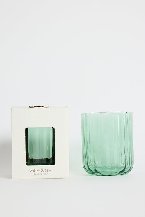 Green glass tumbler in front of its packaging on a white background