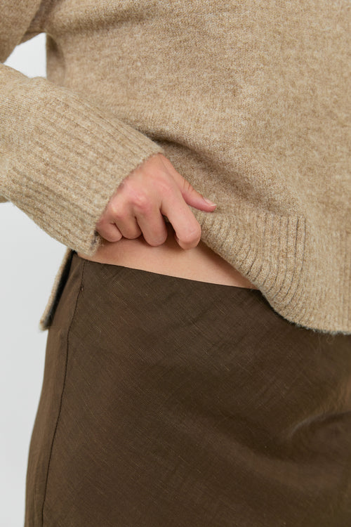 Close-up of a person wearing a beige sweater and brown pants on a white background