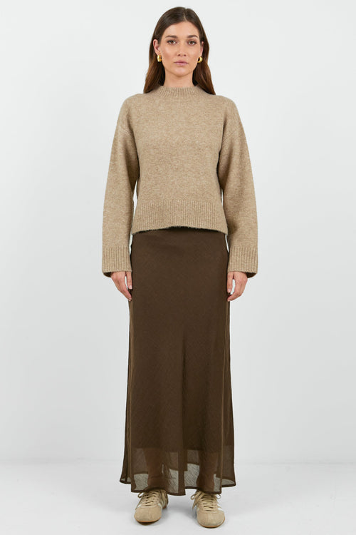 Woman wearing a beige sweater and brown skirt on a white background