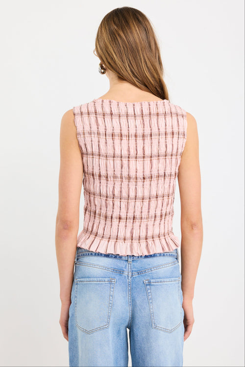 Woman wearing a blush pink sleeveless shirred top with check pattern and frilled hem, styled with light blue wide-leg jeans.