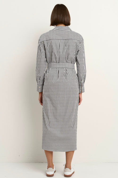 Woman wearing a black and white striped button-down midi shirt dress with a waist tie, rolled sleeves, and white sneakers.