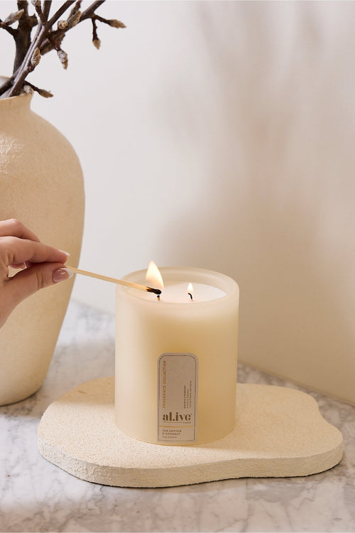 Hand lighting a candle with a decorative vase in the background