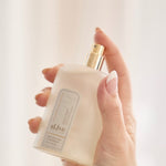 Hand holding a white bottle with a gold cap against a light background