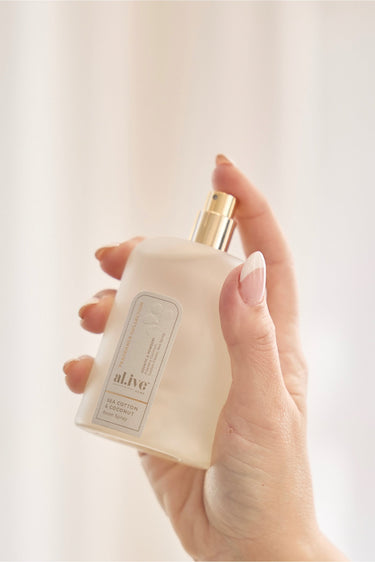 Hand holding a white bottle with a gold cap against a light background