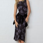 Woman wearing a black floral dress against a white wall