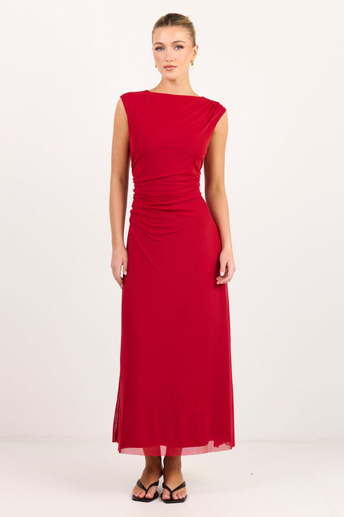 A woman modeling a sleeveless, off-the-shoulder red maxi dress with a gathered waist, standing against a plain white studio background.