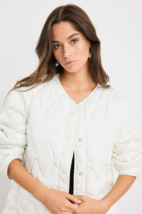 Woman wearing a white quilted jacket on a plain background