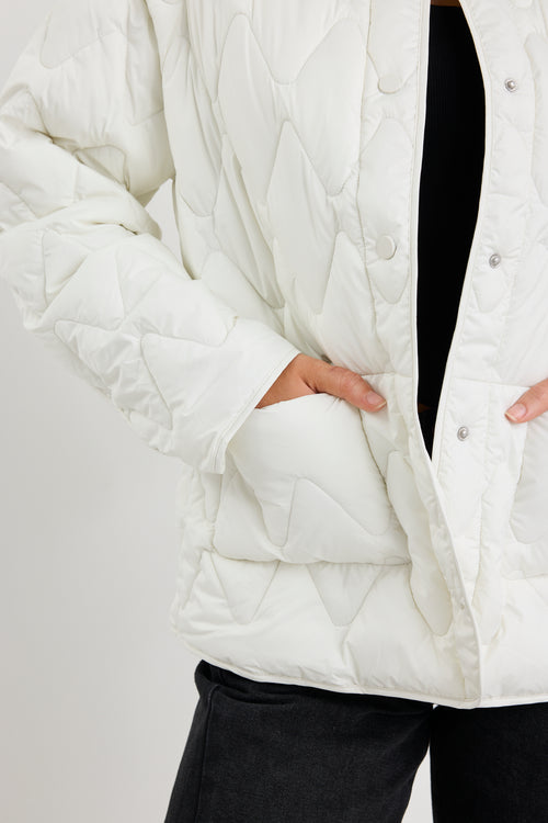 Close-up of a person wearing a white quilted jacket with a plain background