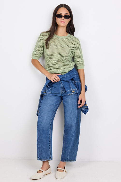 Woman wearing green knit tee and blue denim jeans on white background.