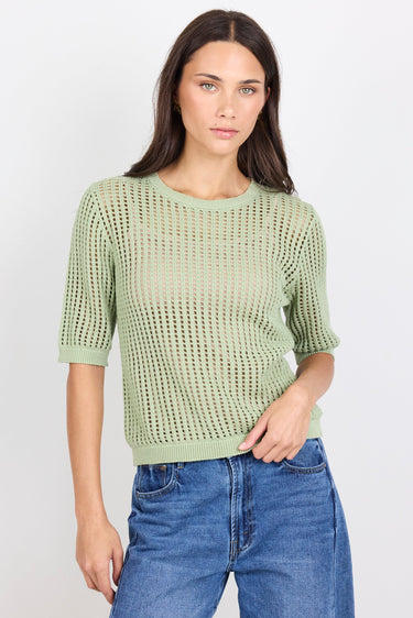 Woman wearing green knit tee and blue denim jeans on white background.