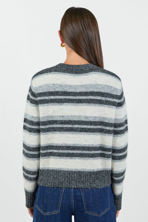 A woman wearing a striped knit cardigan in shades of grey and white with a button-down front, paired with dark blue high-waisted jeans.
