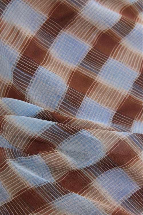 A close-up of a plaid fabric with brown, light blue, and white stripes in a checkered pattern.