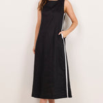 A woman modeling a sleeveless black midi dress with white side stripes, styled with black sunglasses and black sandals against a plain off-white studio background.