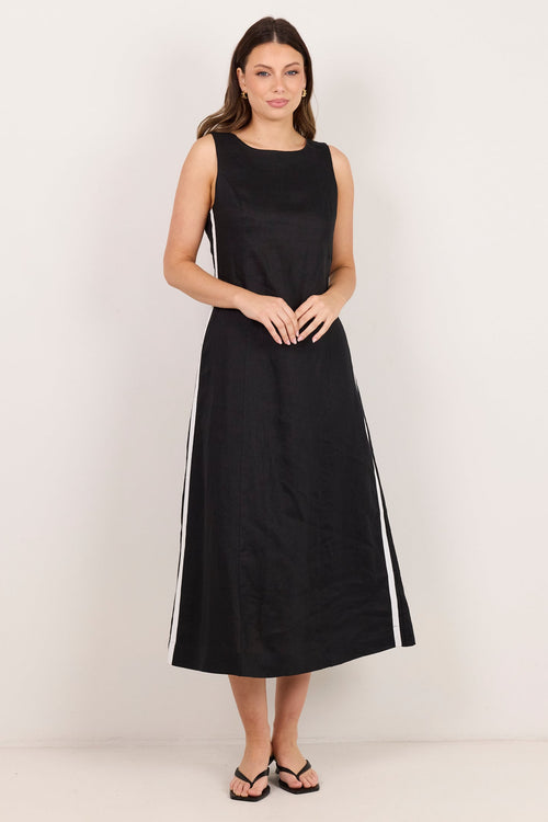 A woman modeling a sleeveless black midi dress with white side stripes, standing against a plain off-white studio background.