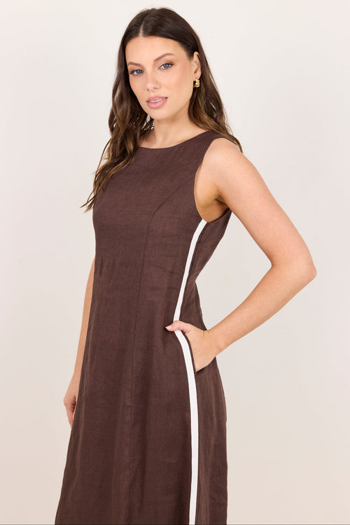 A woman modeling a sleeveless brown dress with a white side stripe, posed against a plain light beige studio background.