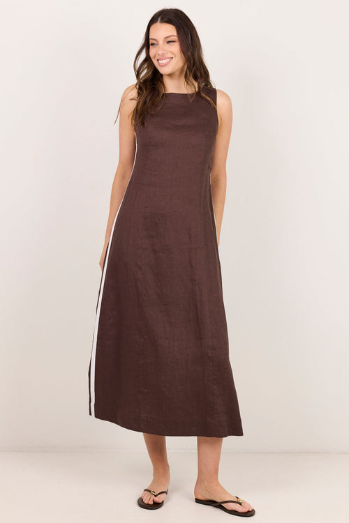 A woman modeling a sleeveless, knee-length brown dress with white side stripes, standing against a plain off-white studio background.