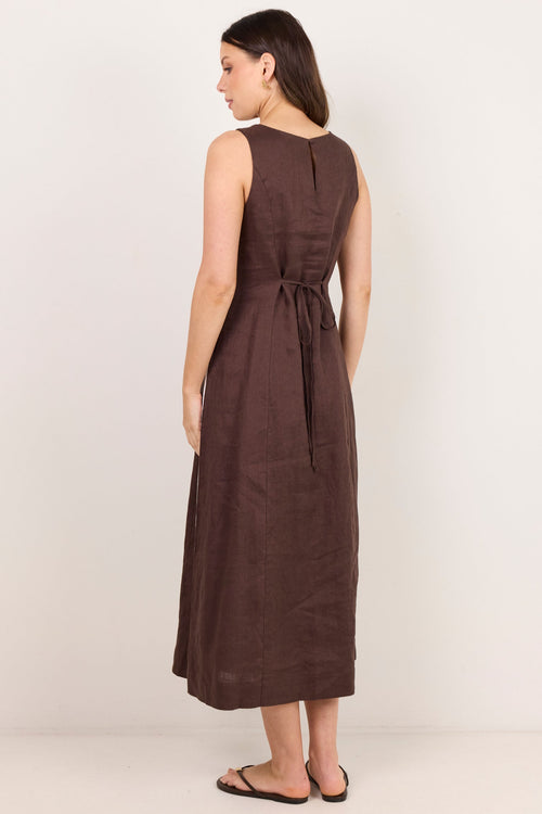 A woman wearing a sleeveless brown midi dress with a tie waist, shown from the back against a plain off-white studio background.