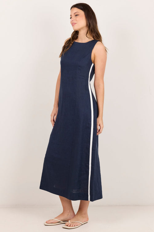 A woman modeling a sleeveless navy blue midi dress with a white side stripe, standing against a plain off-white studio background.