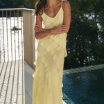 Woman in a yellow dress standing by a pool with trees in the background
