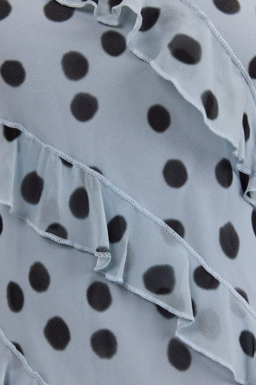 Close-up of a ruffled light gray or pale blue-gray fabric with a black polka dot pattern.