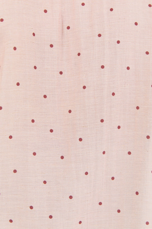A close-up of a light blush pink fabric with a repeating pattern of small, evenly spaced dark red dots.