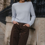 Woman in a light gray sweater and brown pants standing against a black iron gate.