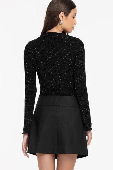 Woman wearing a black polka dot long-sleeve top and black skirt on a white background
