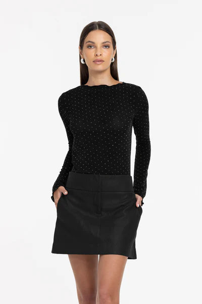 Woman wearing a black polka dot long-sleeve top and black skirt on a white background